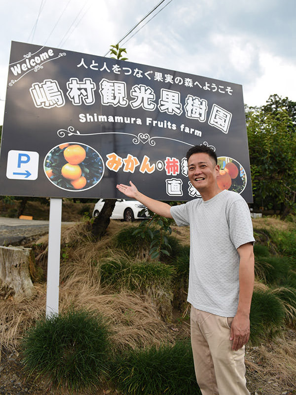 果樹園の看板の前で、嶋村さん